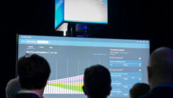 A large screen displays Cascade in front of a crowd of silhouetted heads at a presentation.