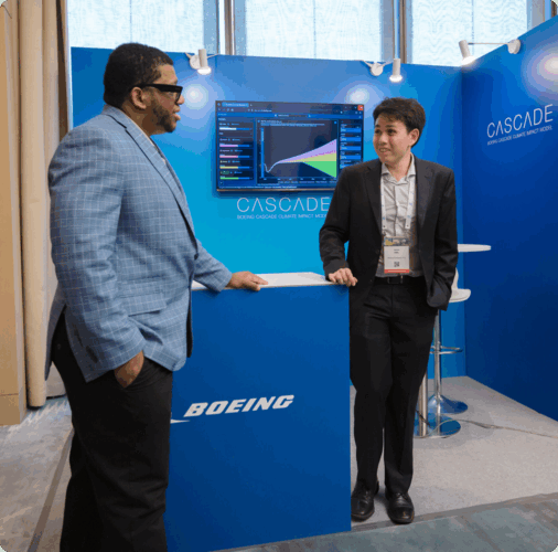 Two people in suits are standing in conversation in front of an event booth with Boeing and Cascade branding.